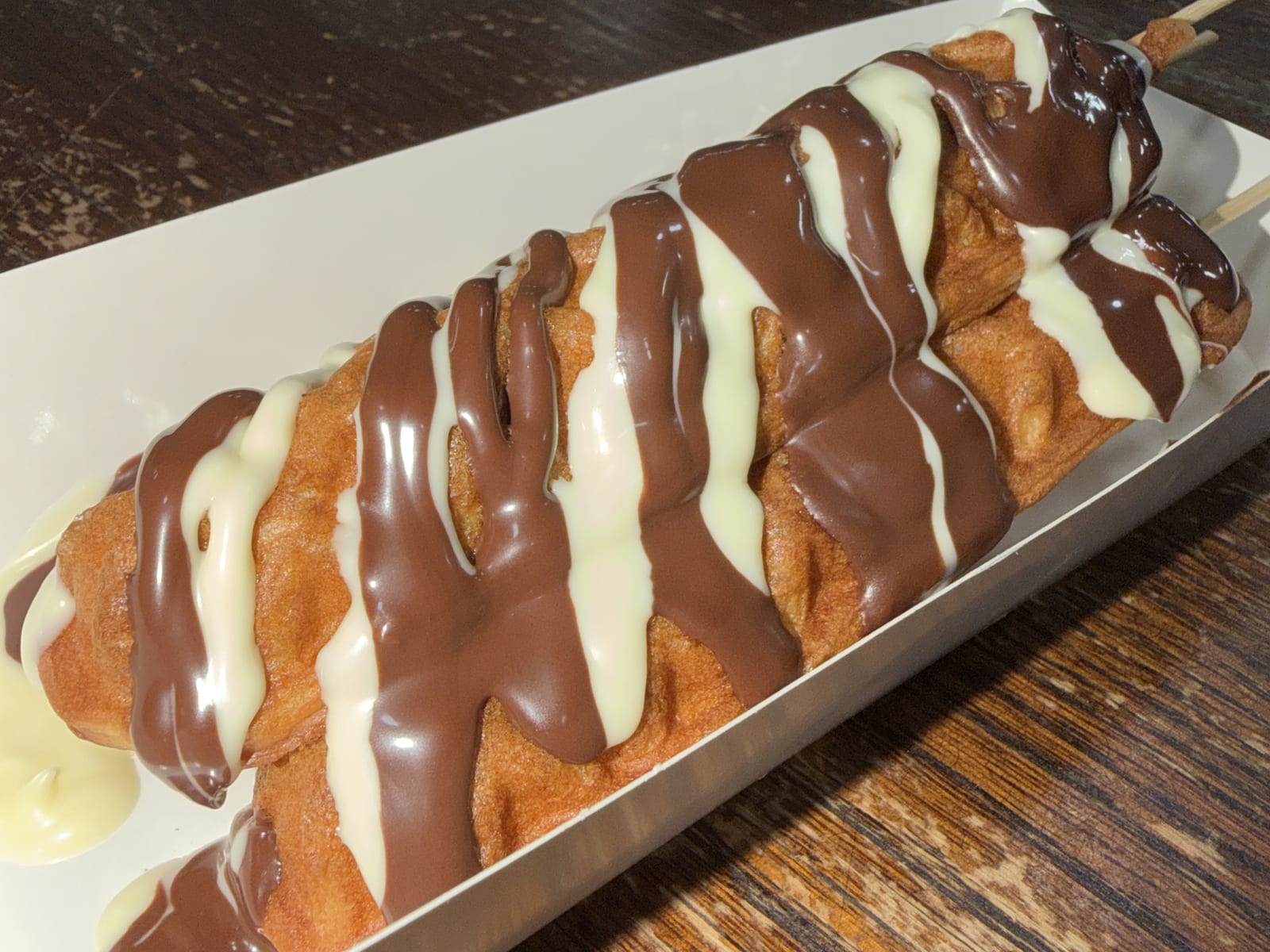 Waffle on a stick finished with milk and white chocolate sauce