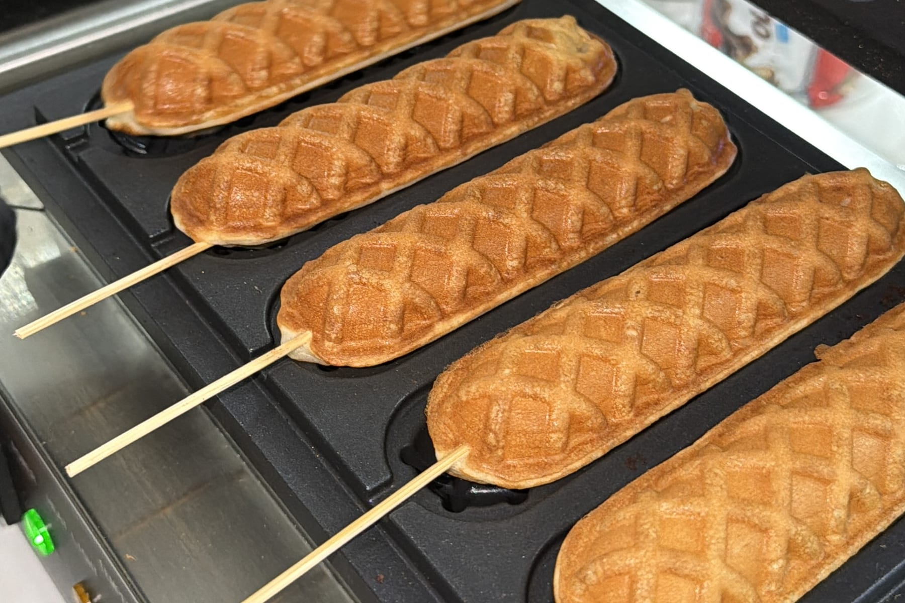 Golden waffles on sticks cooking in the iron at the Sweet St. waffle station